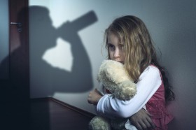 przedstawia przestraszoną małą dziewczynkę z misiem a w tle cień osoby spożywajacej alkohol zdjęcie